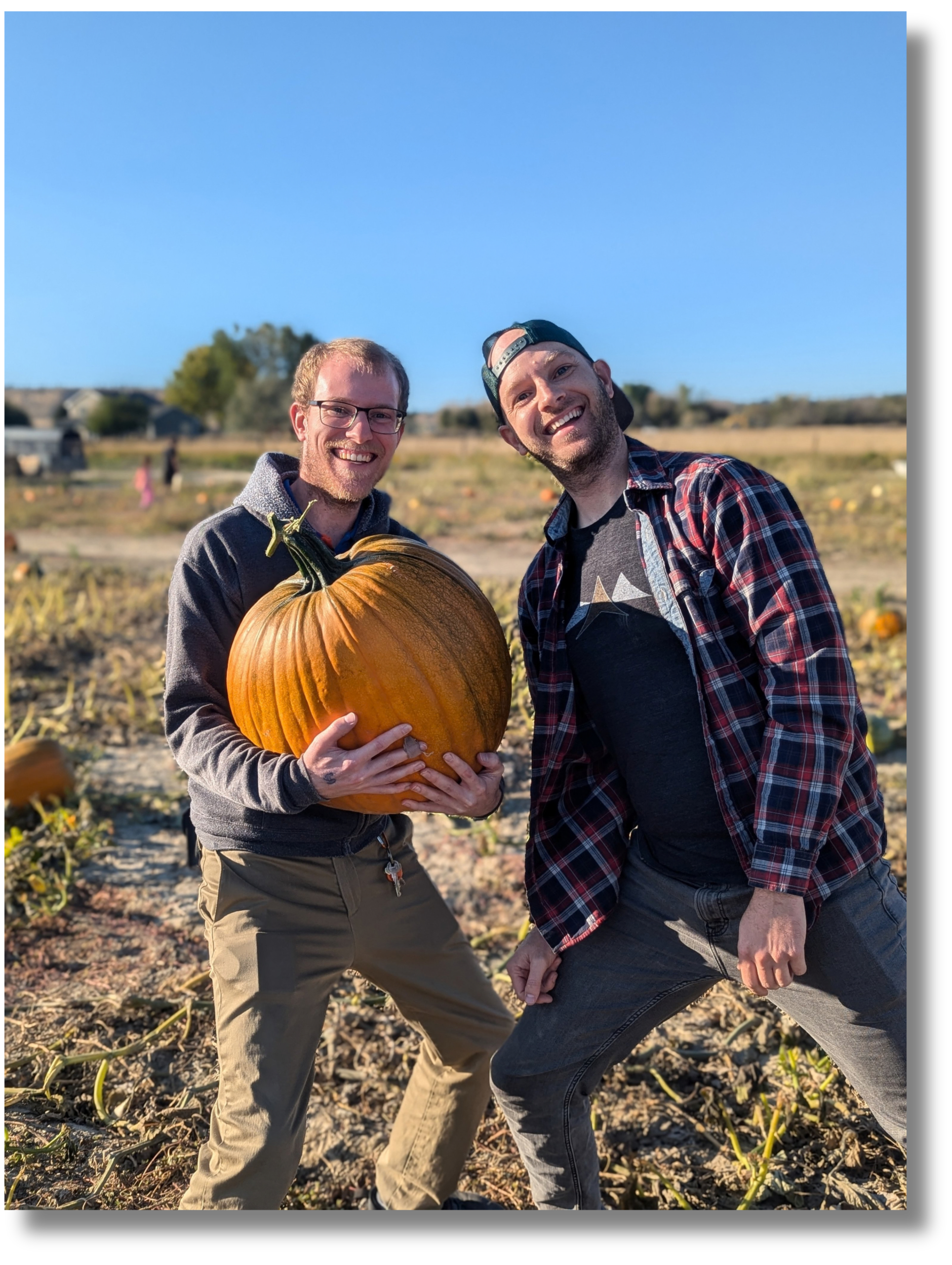 Two friends holding a large pumpkin at a fall pumpkin patch