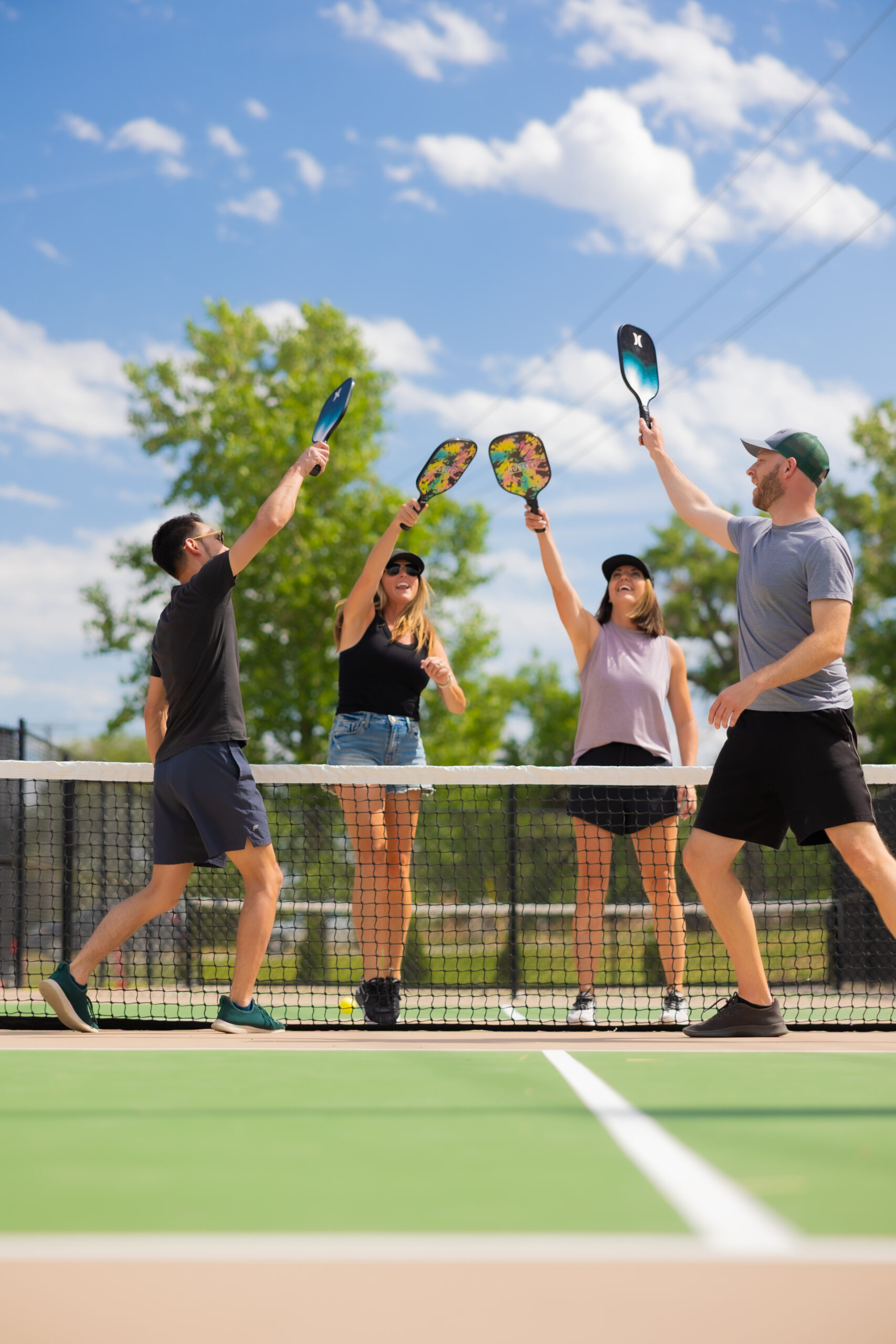 A team of coworkers laughing and playing pickleball together on an outdoor court, enjoying a friendly match that promotes teamwork and motivation.